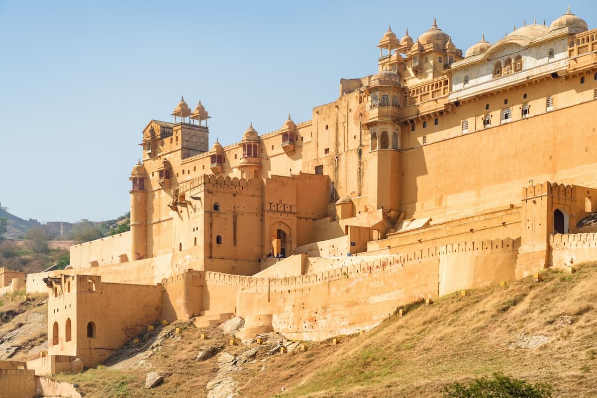 Amer Fort over Maota-sjøen nær Jaipur i Rajasthan — sandsteinsmurer, terrasserte gårder og Aravalli-utløpere.